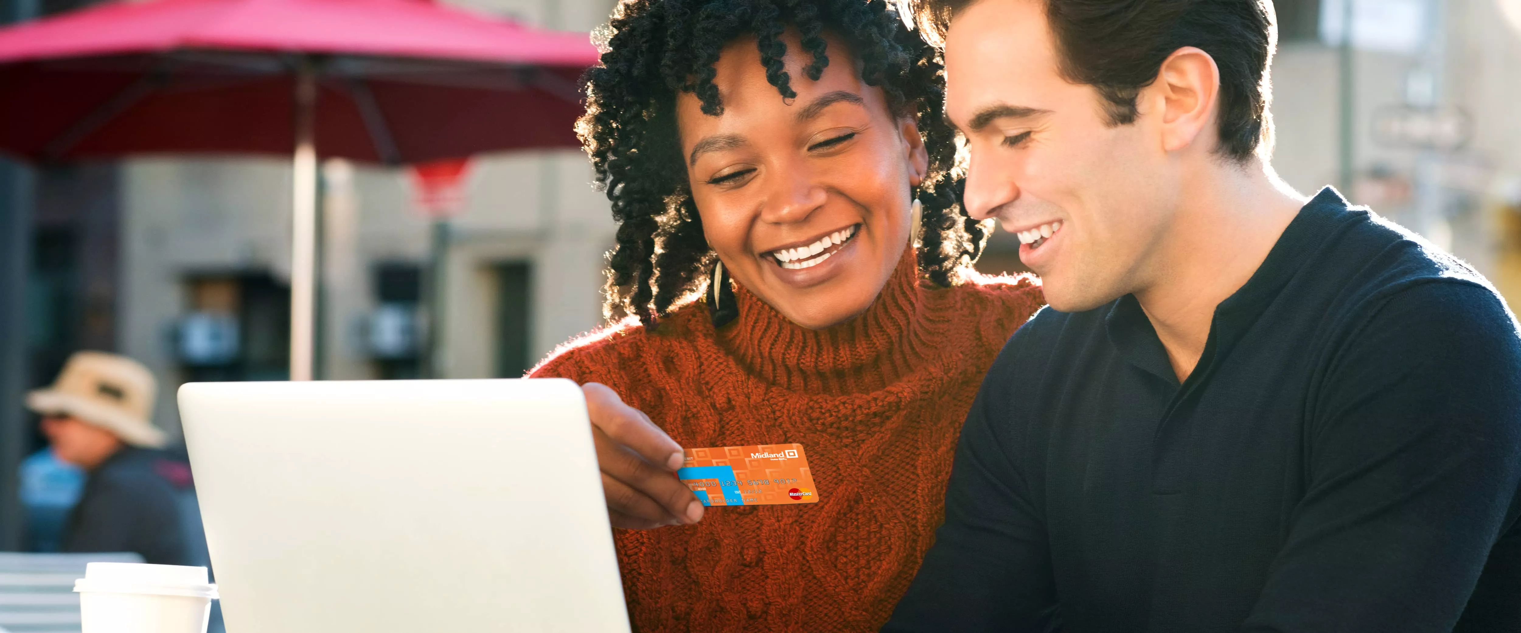 Smiling couple holding a Midland Debit Card while using laptop