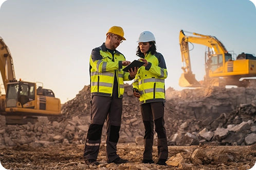 construction workers standing in construction zone talking with machinery behind them