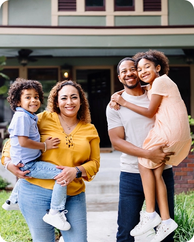 family smiling as they stand outside their new home