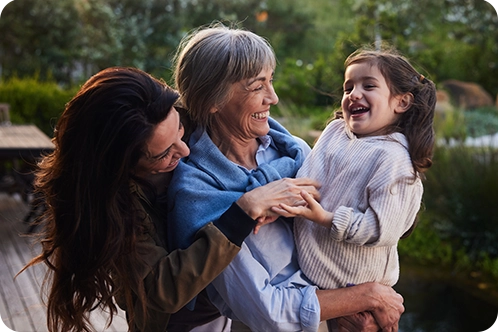 grandmother, mother, and grandchild hugging outside in the yard