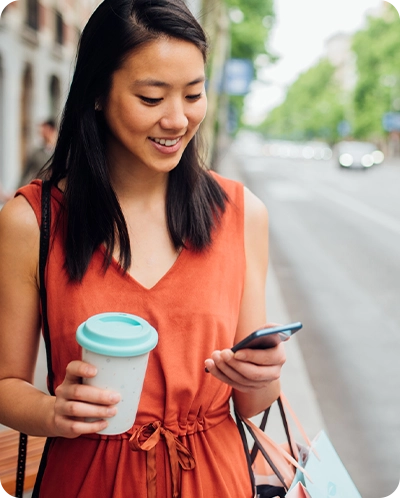 woman smiling as she walks down street and looks at her phone