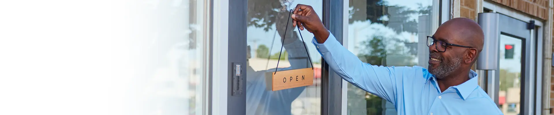 man hanging open sign on his store window